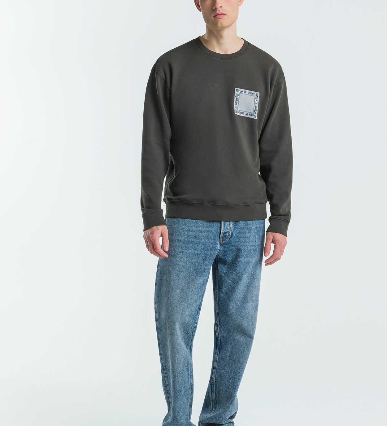 Man wearing a dark grey sweatshirt and blue jeans on a white background