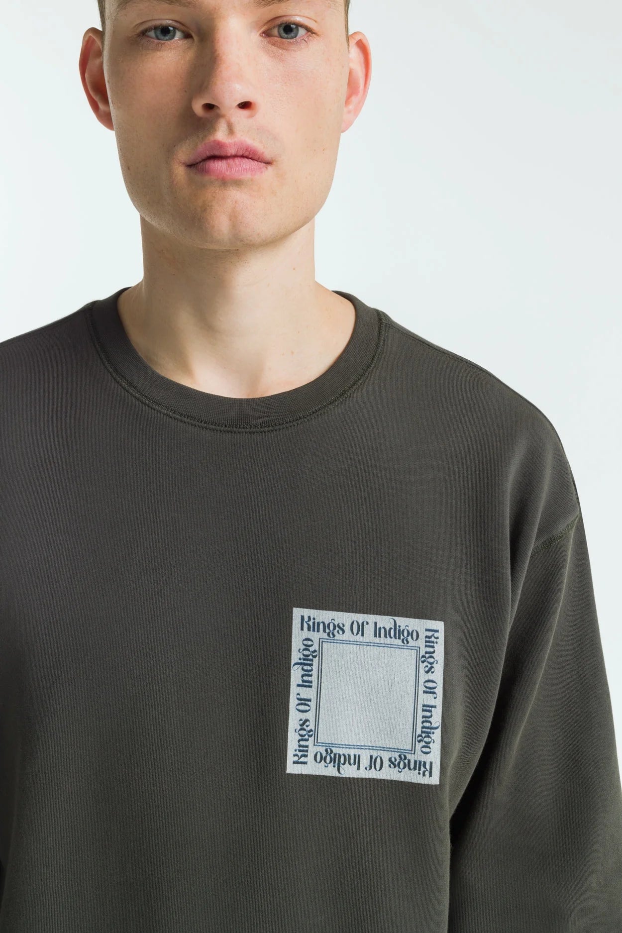 Person wearing a dark grey sweatshirt with a logo on a white background