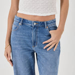 Person wearing blue jeans and a white textured top on a plain background