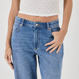 Person wearing blue jeans and a white textured top on a plain background