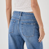 Person wearing blue jeans and a white top on a plain background