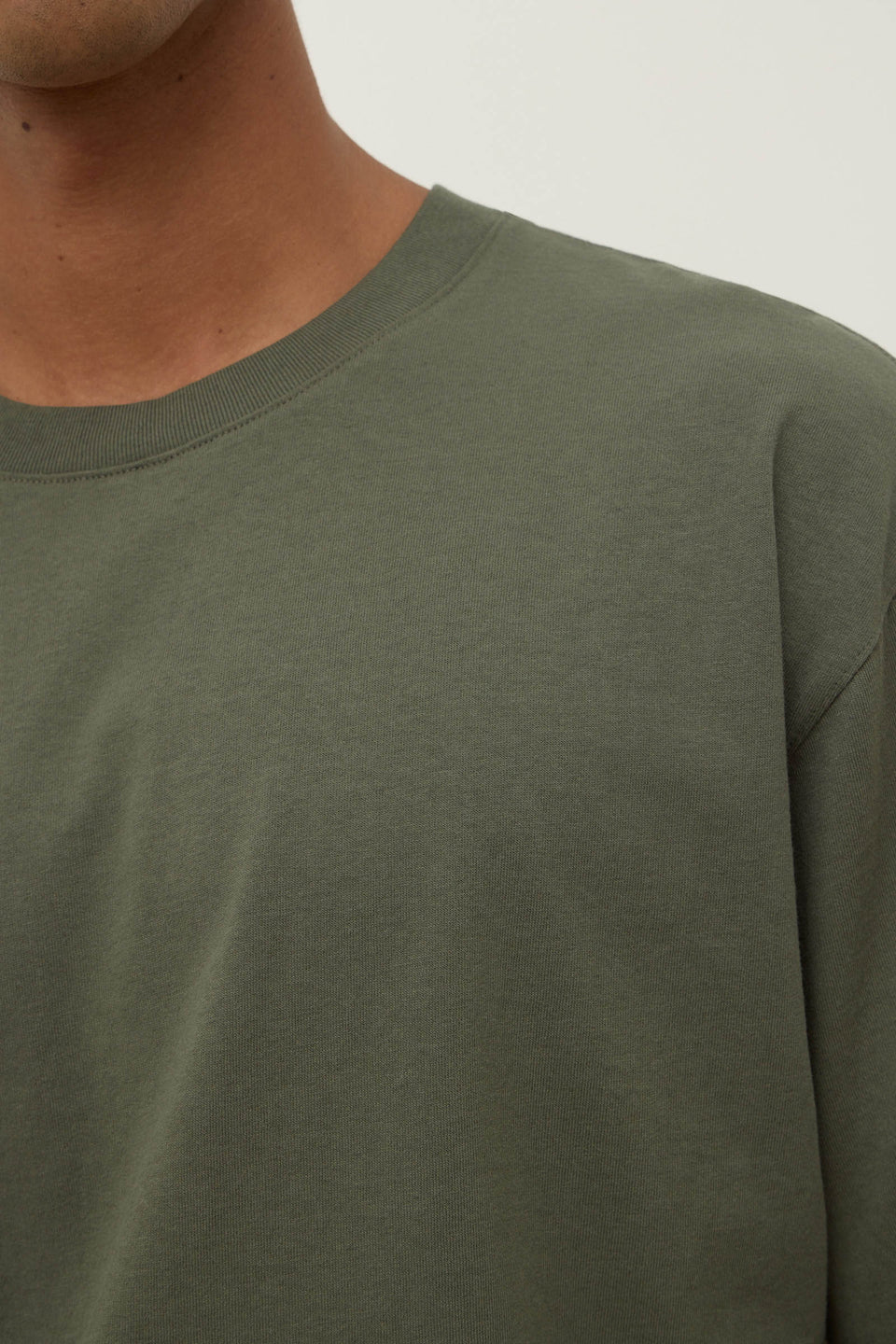 Close-up of a person wearing a green long-sleeve shirt against a neutral background