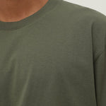 Close-up of a person wearing a green long-sleeve shirt against a neutral background