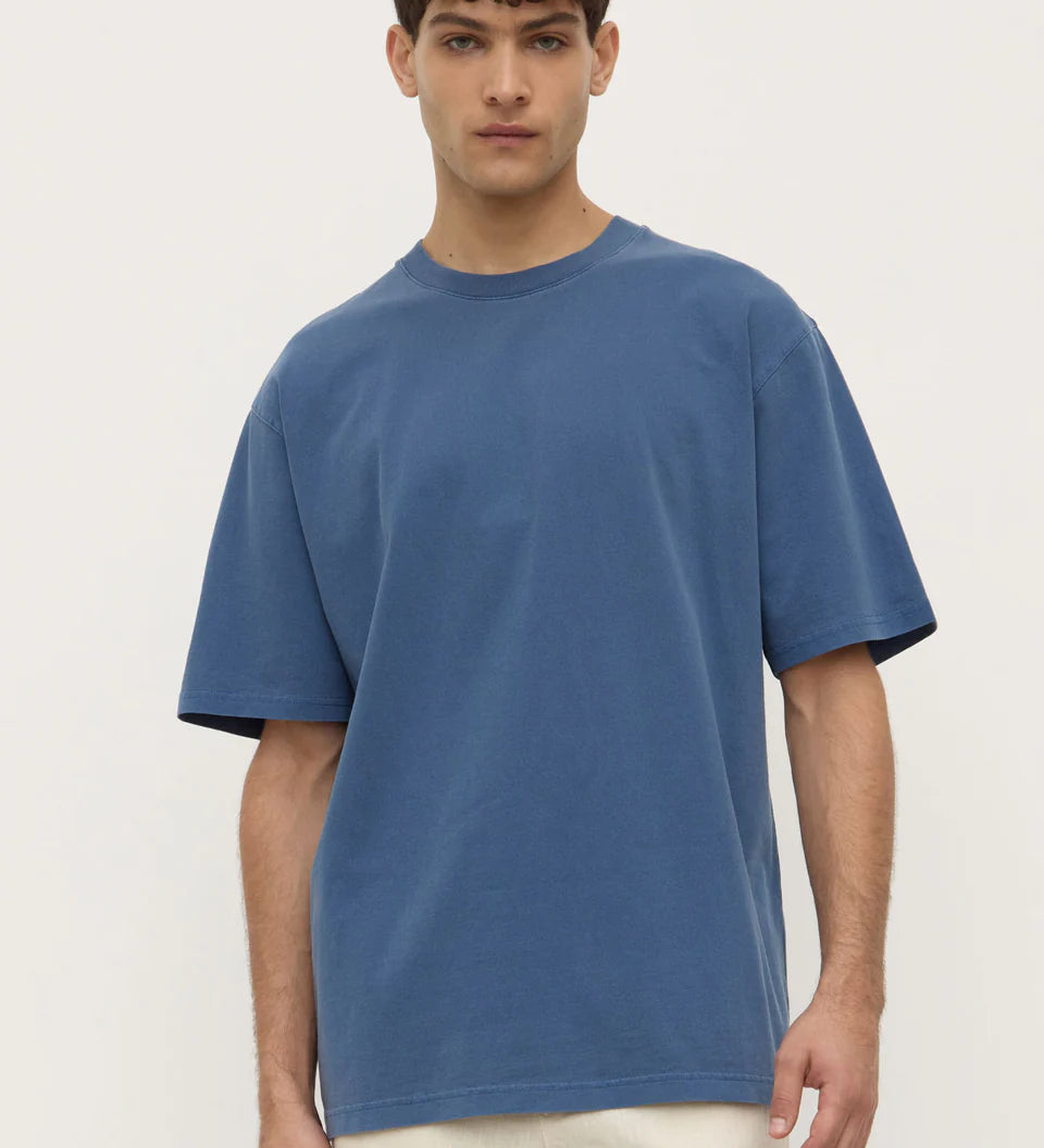 Man wearing a blue t-shirt and white pants against a plain background