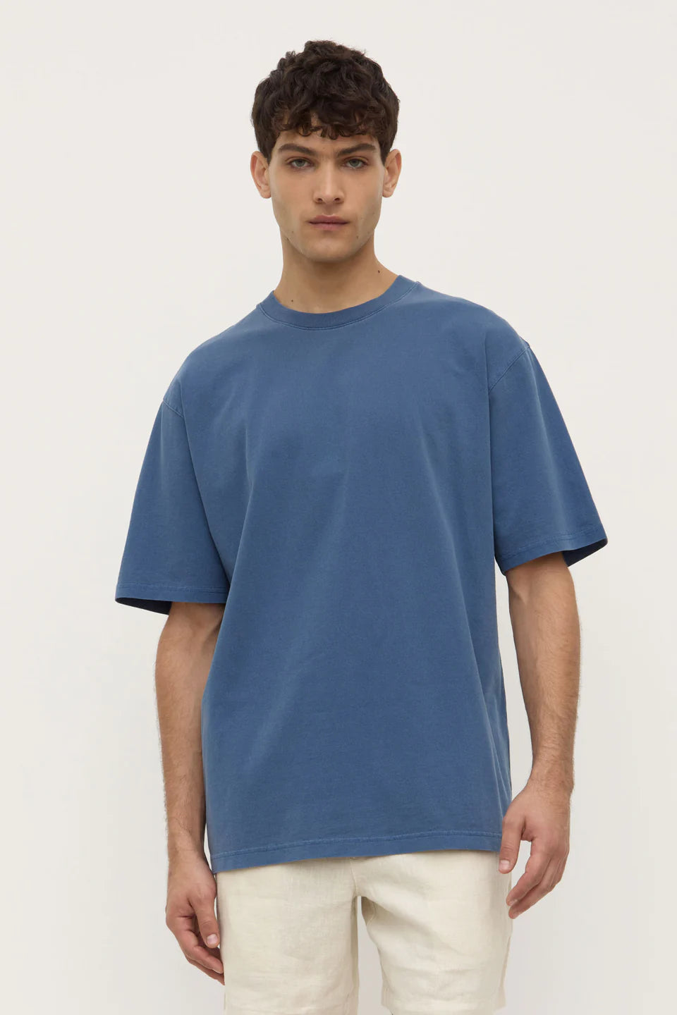 Man wearing a blue t-shirt and white pants against a plain background