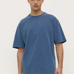 Man wearing a blue t-shirt and white pants against a plain background