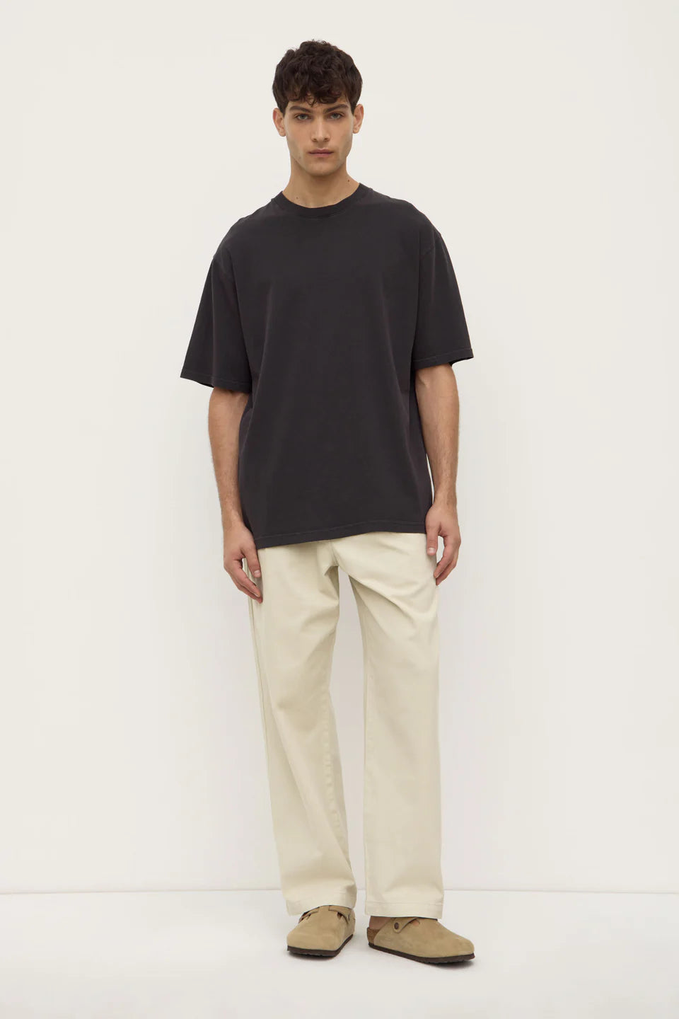 Person wearing a black t-shirt and beige pants on a white background