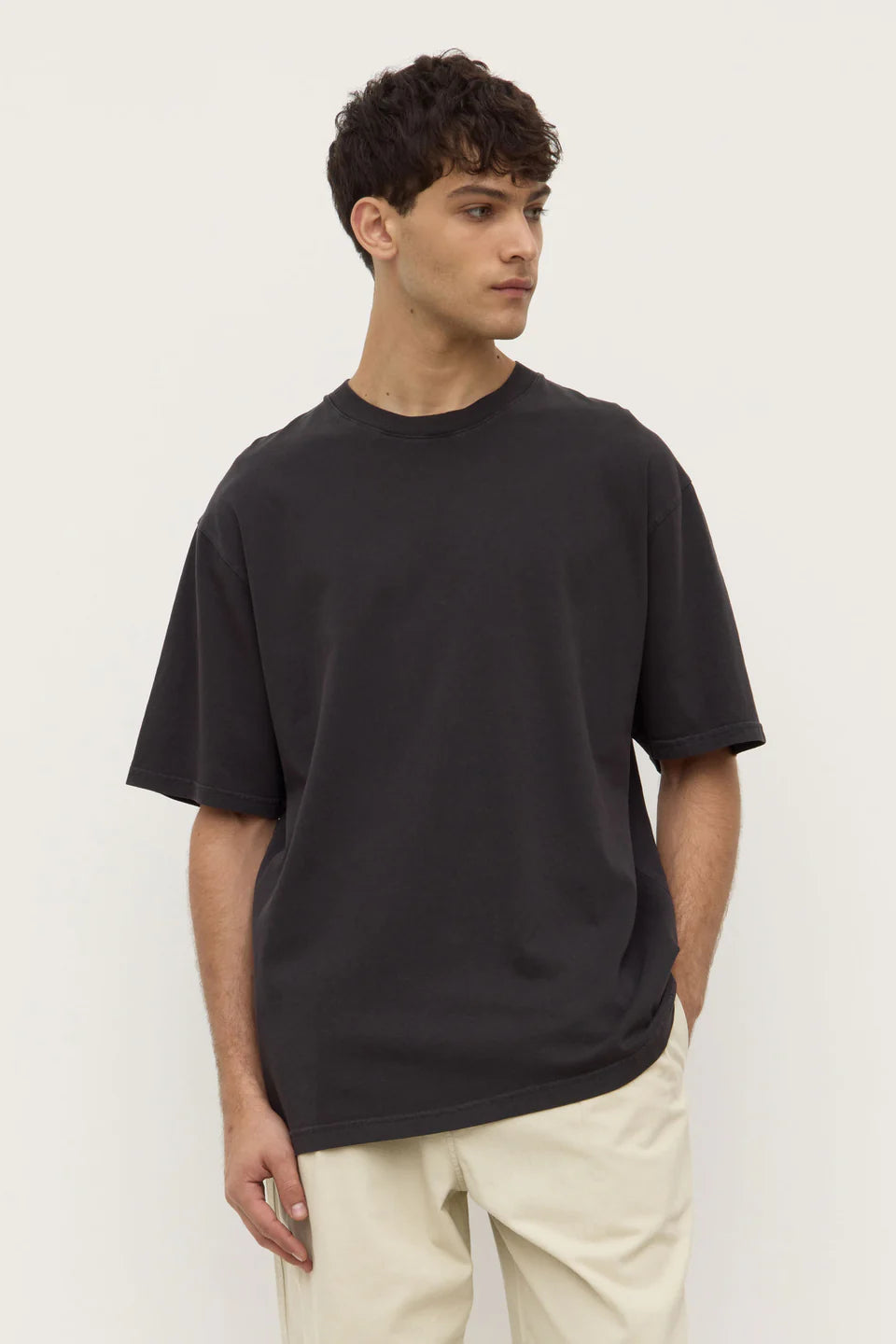 Man wearing a black t-shirt and beige pants against a white background