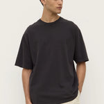 Man wearing a black t-shirt and beige pants against a white background
