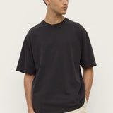 Man wearing a black t-shirt and beige pants against a white background