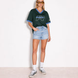 A model stands against a plain white wall wearing a dark green short-sleeve V-neck t-shirt with light blue trim and a large 'R.A.