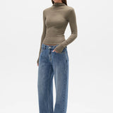 Woman wearing a brown turtleneck and blue jeans on a white background