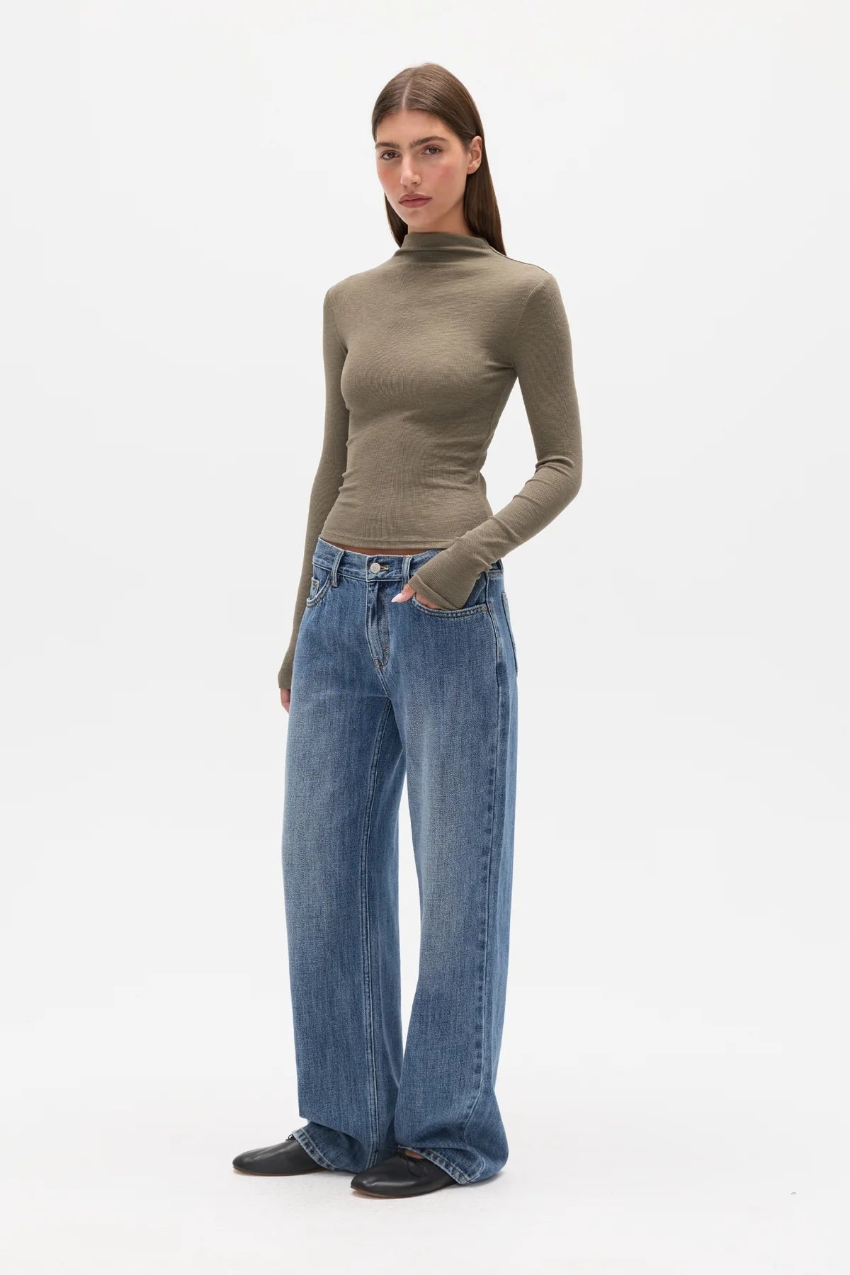 Woman wearing a brown turtleneck and blue jeans on a white background
