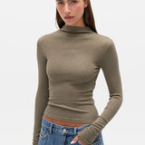 Woman wearing a green turtleneck sweater and blue jeans on a white background