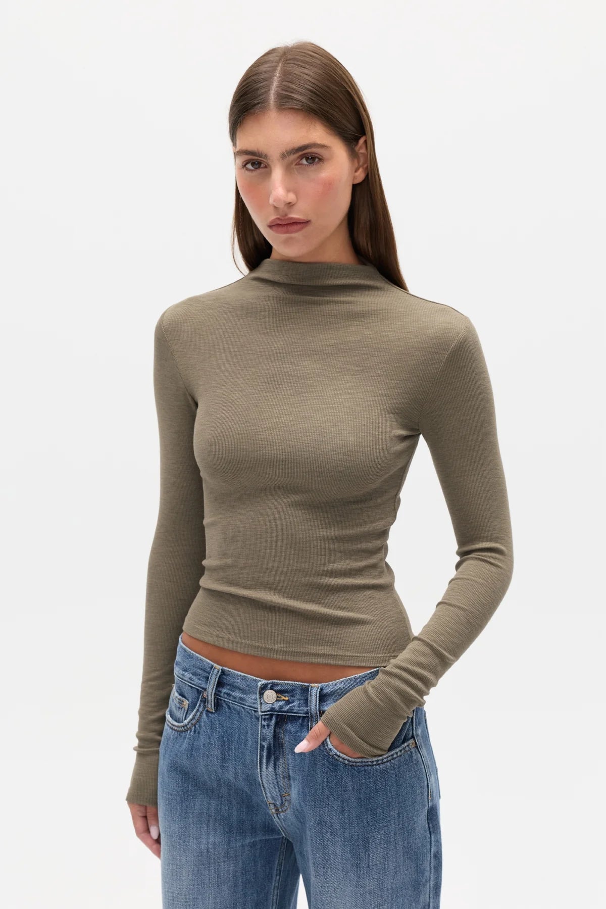 Woman wearing a green turtleneck sweater and blue jeans on a white background