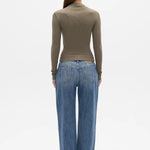 A woman viewed from the back wearing a fitted olive-brown long-sleeve mock-neck top and wide-leg blue jeans against a plain white studio background.