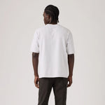 A man viewed from behind wearing a plain white short-sleeve t-shirt and dark cargo pants, standing against a light gray studio background.