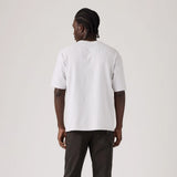 A man viewed from behind wearing a plain white short-sleeve t-shirt and dark cargo pants, standing against a light gray studio background.