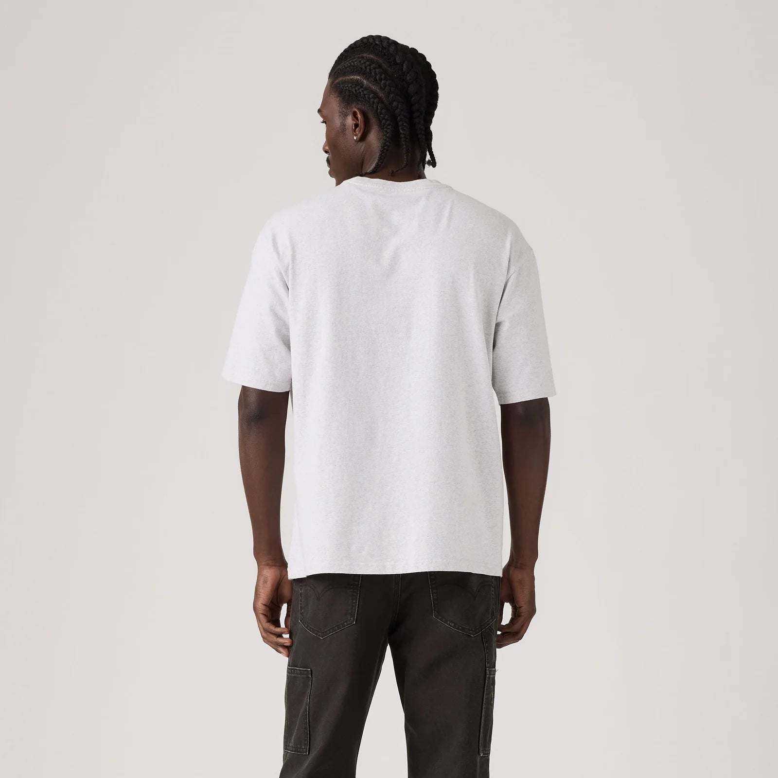 A man viewed from behind wearing a plain white short-sleeve t-shirt and dark cargo pants, standing against a light gray studio background.