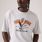 A man wearing a light gray crewneck t-shirt with a vintage-style graphic of a goose and the text 'IN OUR FIELD OF WORK We fly by the seat of our pants'.