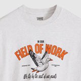 A close-up of a light heather gray Levi's t-shirt featuring a vintage-style graphic print with orange text reading 'FIELD OF WORK', a flying duck, and black script text below.