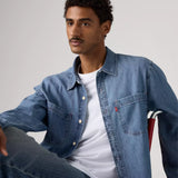 Man wearing a blue denim jacket over a white shirt on a gray background