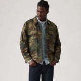 Person wearing a camouflage jacket over a denim shirt on a plain background