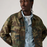Man wearing a camouflage jacket over a denim shirt on a plain background