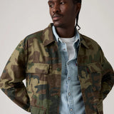 Man wearing a camouflage jacket over a denim shirt on a plain background
