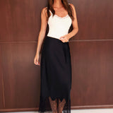 Woman wearing a white top and black skirt with lace details against a brown wall.