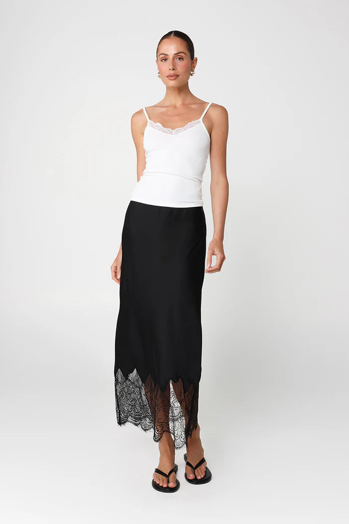 Woman wearing a white top and black skirt with lace hem on a white background
