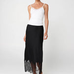 Woman wearing a white top and black skirt with lace hem on a white background
