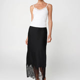 Woman wearing a white top and black skirt with lace hem on a white background