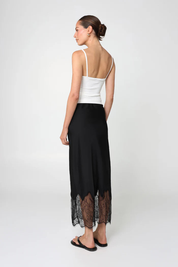 Woman wearing a white top and black pants with lace details on a white background
