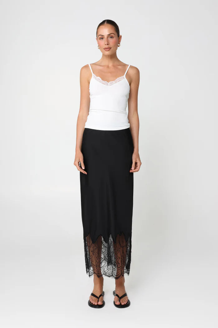 Woman wearing a white top and black skirt with lace hem on a white background