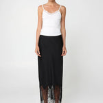 Woman wearing a white top and black skirt with lace hem on a white background