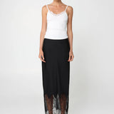 Woman wearing a white top and black skirt with lace hem on a white background