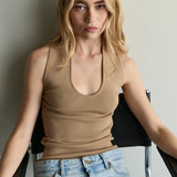 Woman wearing a beige tank top and blue jeans sitting on a chair against a plain background