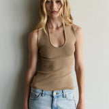 Woman wearing a beige tank top and light blue jeans against a plain background