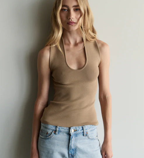 Woman wearing a beige tank top and light blue jeans against a plain background