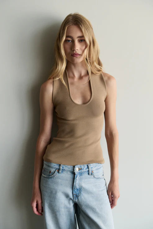 Woman wearing a beige tank top and light blue jeans against a plain background