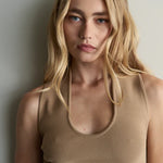 Woman wearing a beige sleeveless top against a plain background