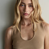 Woman wearing a beige sleeveless top against a plain background
