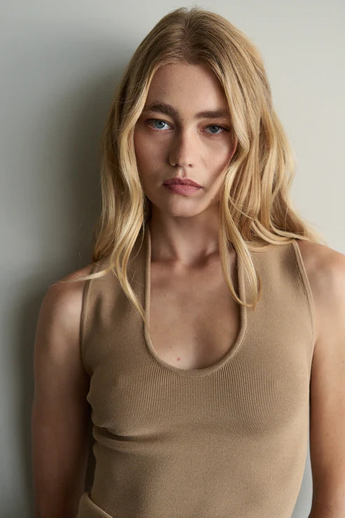 Woman wearing a beige sleeveless top against a plain background
