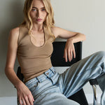 Woman sitting on a chair wearing a beige tank top and light blue jeans.