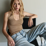 Woman sitting on a chair wearing a beige tank top and light blue jeans.