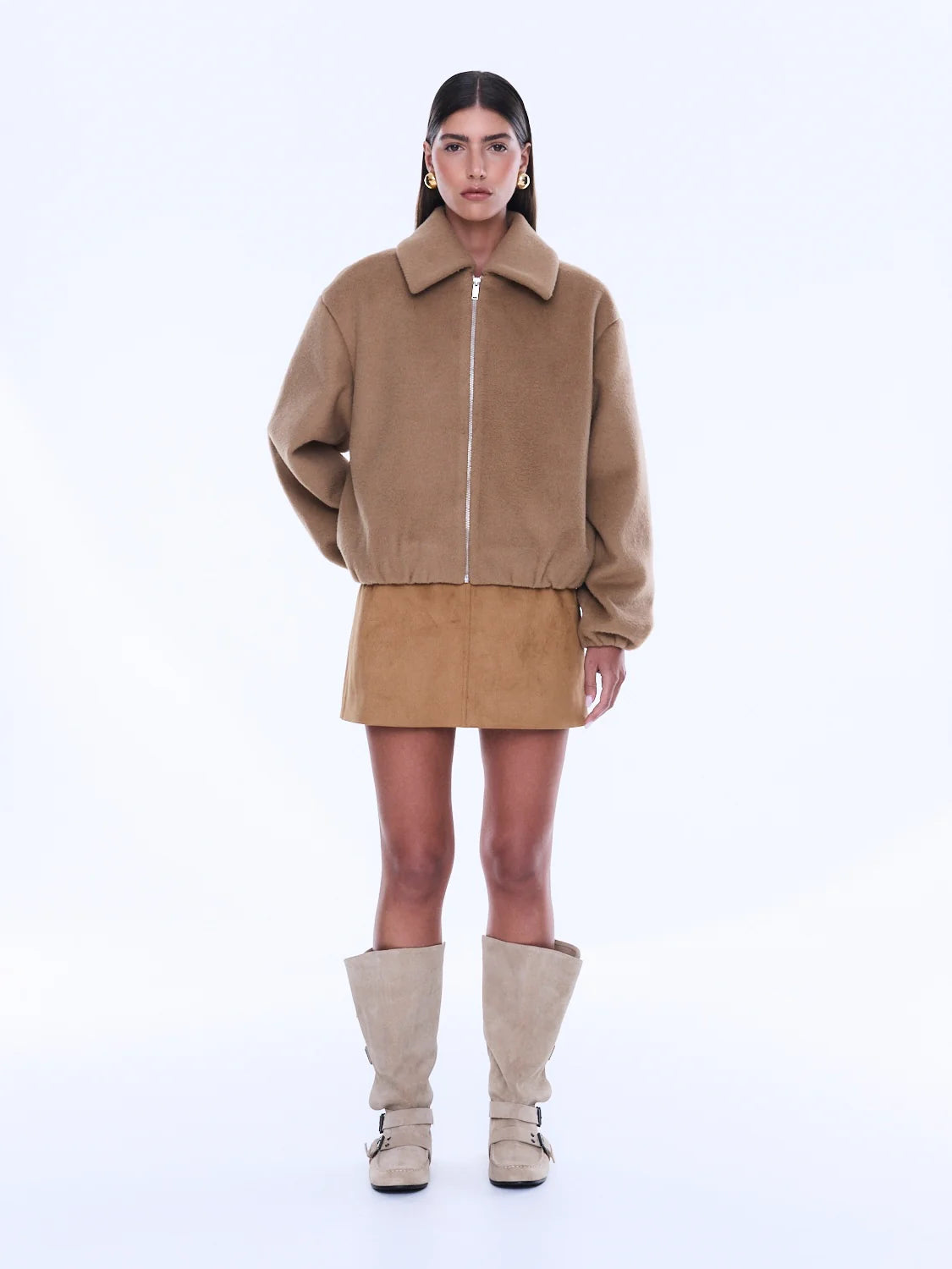 Woman wearing a beige jacket and skirt with knee-high boots on a white background