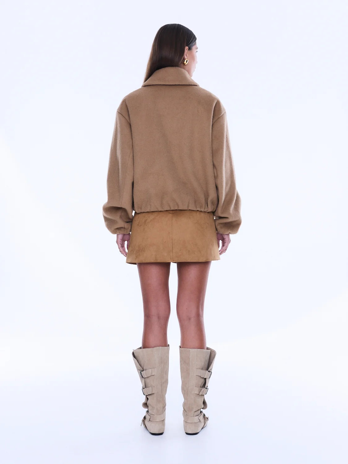 Person wearing a beige jacket and skirt set with high-heeled boots on a white background
