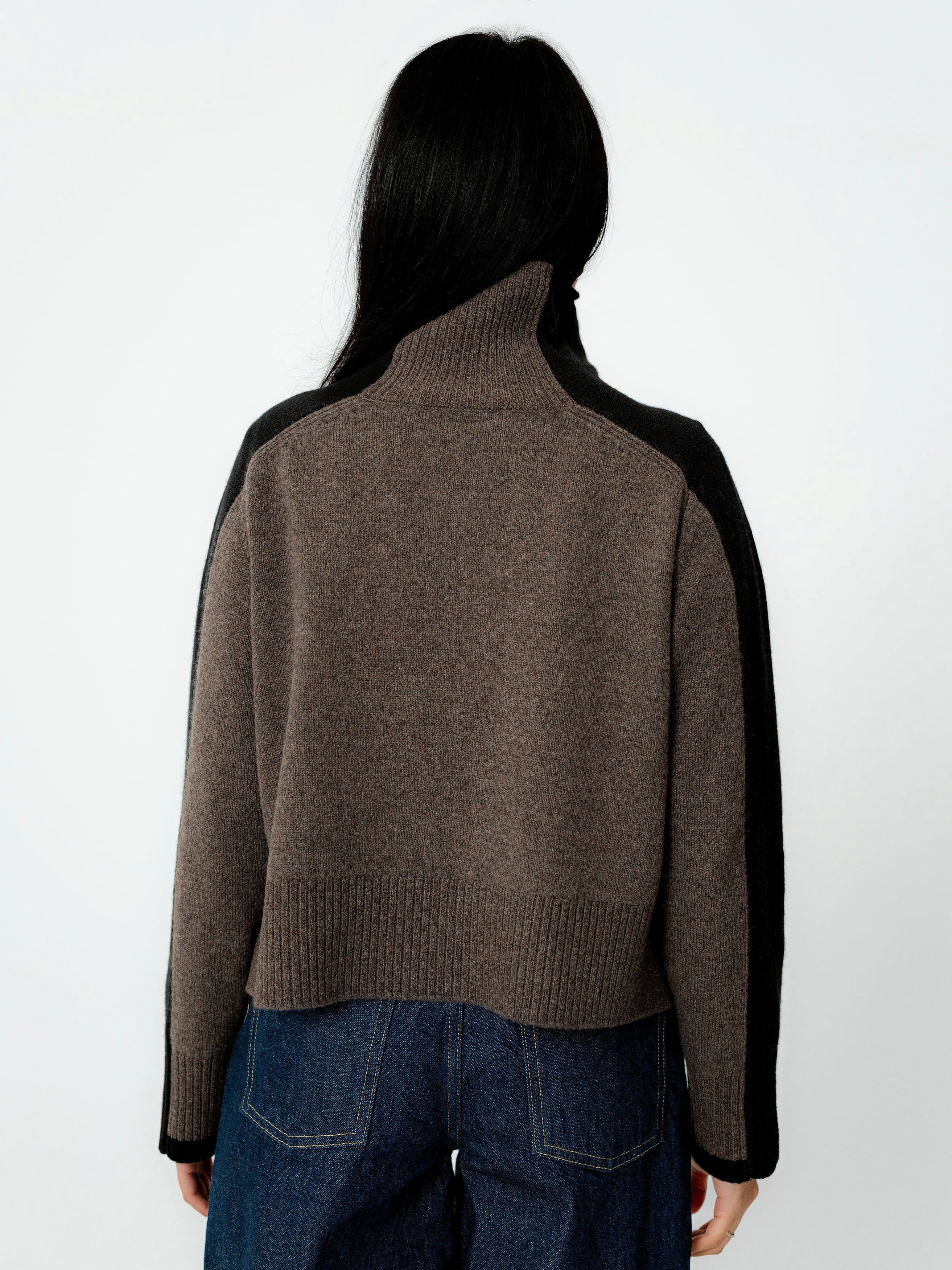 Person wearing a brown sweater with black sleeves on a white background