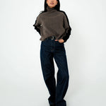 Person wearing a brown turtleneck sweater and dark jeans on a white background